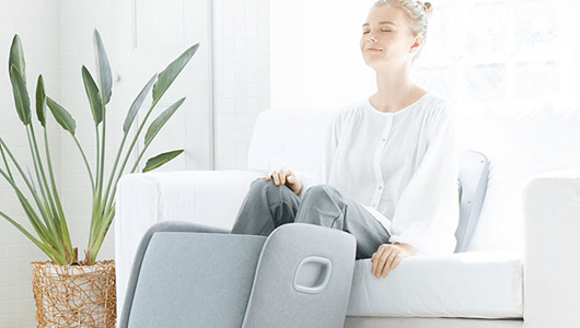 Woman using the Synca REI foot massager, sitting on a couch