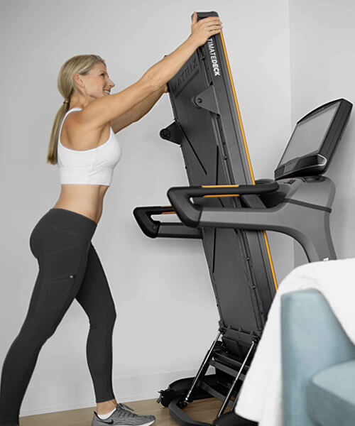 Woman folding Matrix treadmill in guest room