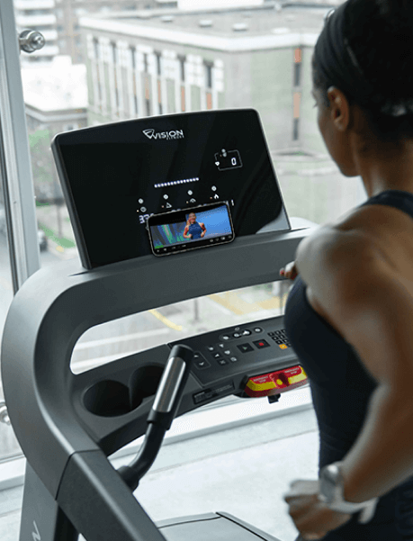 Woman running on Vision treadmill using Treo app on phone